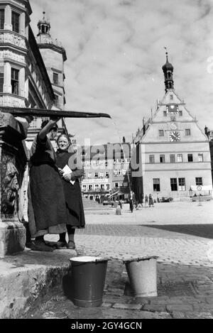 Zwei Frauen unterhalten sich während Sie die Wassereimer mit Wasser aus dem Springbrunnen Am Marktplatz vor dem Rathaus und der Ratstrinkstube voll laufen lassen, Rothenburg ob der Tauber, Deutschland 1930er Jahre. Due donne aventi una chat mentre il bucktes sono il riempimento con acqua dalla fontana posta nella piazza del mercato vicino al municipio e Ratstrinkstube a Rothenburg ob der Tauber, Germania 1930s. Foto Stock