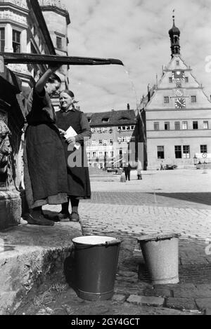 Zwei Frauen unterhalten sich während Sie die Wassereimer mit Wasser aus dem Springbrunnen Am Marktplatz vor dem Rathaus und der Ratstrinkstube voll laufen lassen, Rothenburg ob der Tauber, Deutschland 1930er Jahre. Due donne aventi una chat mentre il bucktes sono il riempimento con acqua dalla fontana posta nella piazza del mercato vicino al municipio e Ratstrinkstube a Rothenburg ob der Tauber, Germania 1930s. Foto Stock
