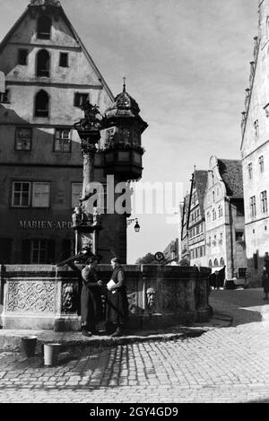 Zwei Frauen unterhalten sich während Sie die Wassereimer mit Wasser aus dem Springbrunnen vor dem imposanten Rathaus voll laufen lassen, Rothenburg ob der Tauber, Deutschland 1930er Jahre. Due donne aventi una chat mentre il bucktes sono il riempimento con acqua dalla fontana posta di fronte all'imponente Municipio di Rothenburg ob der Tauber, Germania 1930s. Foto Stock