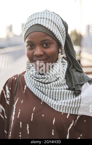 Primo piano della giovane musulmana africana che sorride alla macchina fotografica mentre si trova all'aperto Foto Stock