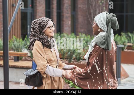 Due donne musulmane che tengono le mani e sorridono l'una all'altra durante il loro incontro in città Foto Stock
