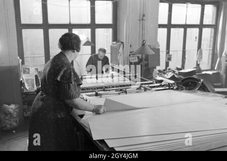 Eine Druckereimitarbeiterin legt die bedruckten Papierbögen in eine Planschneidemaschine produziert vom Maschinenbaukonzern MAN (Maschinenfabrik Augsburg-Nürnberg), Deutschland 1930er Jahre. Un lavoratore in una printery sta mettendo la carta stampata in fogli all'interno di una macchina di taglio, che viene prodotta mediante l'ingegneria meccanica azienda MAN (Maschinenfabrik Augsburg-Nürnberg), Germania 1930s. Foto Stock