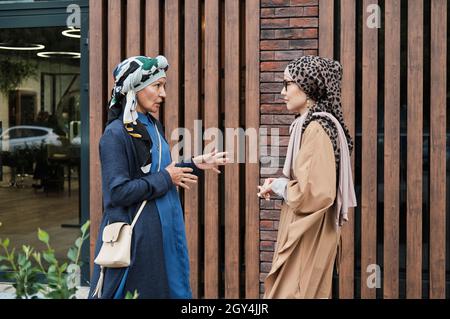 Due donne musulmane in abbigliamento tradizionale che si comunicano tra loro mentre si incontrano nel centro della città Foto Stock