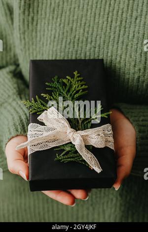 Le mani femminili che tengono la scatola del regalo piacevole. Donna che dà avvolto in carta nera presente. Accogliente design a confezione regalo Foto Stock