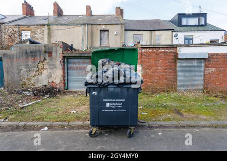 Gateshead UK: 6 marzo 2021: Un bidone a ruota pieno nel vicolo posteriore Grimy in Gateshead Inghilterra Foto Stock