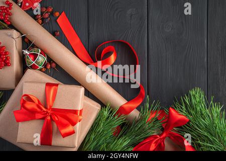 Regali di Natale, rami di abete e carta da imballaggio su sfondo scuro. Vista dall'alto, spazio di copia. Foto Stock