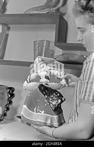 Die Angestellte auf einem Messestand für Porzellan und Keramik mit einer Porzellanfigur auf der Messe Leipzig, Deutschland 1940er Jahre. Una femmina di membro dello staff in uno stand per porcellana e ceramica con una statuetta in Leipzig trade show, Germania 1940s. Foto Stock