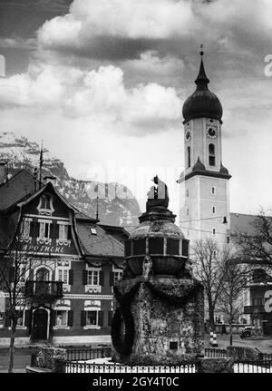 La fotografia mostra l'Alte Apotheke (casa no 10), il memoriale di guerra e la chiesa parrocchiale di San Martino in Marienplatz a Garmisch nel febbraio 1936, presumibilmente prima del 4 febbraio, quando la neve sperata cadde per l'apertura delle Olimpiadi invernali il 6 febbraio. Sullo sfondo ci sono la testa del gatto e il piedistallo del re. [traduzione automatizzata] Foto Stock