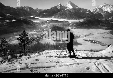 Un giovane sciatore negli anni trenta si affaccia da Marxenhöhe sulla città di Berchtesgaden e la catena alpina (da sinistra a destra): Funtenseetauern, Schönfeldspitze, Watchmann, Grünstein (direttamente di fronte), Hochkalter. Sopra la Königssee ci sono nubi di nebbia. Di fronte al Lockstein (collina boscosa in primo piano) si vede il vecchio ospedale distrettuale. [traduzione automatizzata] Foto Stock