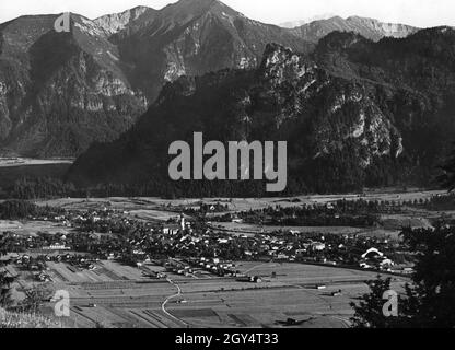 Questa fotografia non scattata, probabilmente scattata intorno al 1930, mostra il villaggio di Oberammergau nella valle attraverso la quale scorre la raddrizzata Ammer. L'edificio più grande al bordo del villaggio sulla sinistra è la scuola di scultura. Sullo sfondo sorge l'Ammergebirge con il Kofel (centro della foto) e con Ziegelspitz e Notkarspitze alle sue spalle. [traduzione automatizzata] Foto Stock