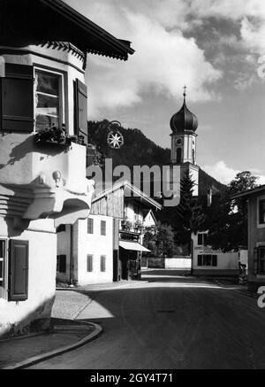 'Questa foto non ancora scattata, probabilmente scattata intorno al 1930, mostra il Dorfstraße di Oberammergau all'angolo con la Sterngasse (a sinistra). All'angolo, l'Oriel appende il cartello con il naso del ''Gasthaus zum Stern'''. Sull'altro lato della strada, poco prima della chiesa di San Pietro e Paolo, si trova il negozio di ''Inh. Franziska Gerstl née Zwink'', che offre 'Schnitt- Kurz u. [...] / Wäsche Trachten[...]'. [traduzione automatizzata]' Foto Stock