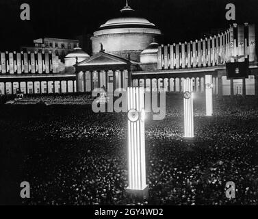 Una folla si è riunita nella luminosa Piazza del Plebiscito di Napoli la sera del 5 maggio 1938. L'occasione è stata Fleet Day in città. Sullo sfondo si trova la chiesa di San Francesco di Paola. Sulle colonne si trovano i seguenti simboli (dalla parte anteriore a quella posteriore): Stemma del Regno d'Italia, swastika, Fascis del Partito Nazionale fascista. [traduzione automatizzata] Foto Stock