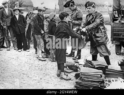 Due giovani leader fascisti dell'Opera Nazionale Balilla consegnano le uniformi ai bambini la domenica per una lunga marcia di gruppo. La foto è stata scattata nel 1933 nei pressi di Latina nella pianura pontina. I ragazzi sono figli di contadini che sono stati sistemati nella zona sgocciolata. [traduzione automatizzata] Foto Stock