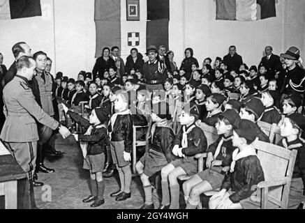 I ragazzi ricevono le loro carte da un ufficiale dell'organizzazione giovanile fascista Opera Nazionale Balilla nel 1933. Il ragazzo a sinistra solleva il braccio nel saluto romano. L'evento si svolge in una Casa del Balilla, le case dell'Opera Nazionale Balilla in Italia. [traduzione automatizzata] Foto Stock