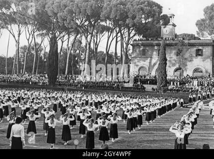 'Nel 1936 l'Opera Nazionale Balilla ha tenuto una manifestazione di ginnastica in Piazza di Siena nel Parco di Villa Borghese a Roma. Le ragazze della ''giovani Italiane'' hanno eseguito gli esercizi provati sul campo sportivo secondo le istruzioni dei capigruppo. Sullo sfondo, gli spettatori hanno allineato gli stand. Alle spalle si trova il Casinò dell'orologio. [traduzione automatizzata]' Foto Stock