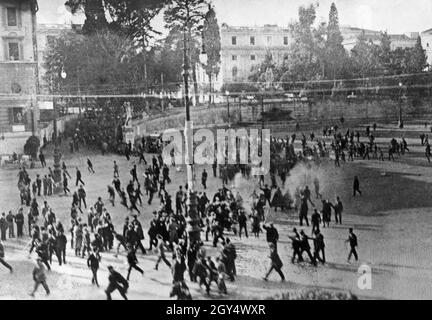 Scontri e rivolte scoppiarono a Roma nel 1924 il 4 novembre, giorno delle celebrazioni della Giornata della Vittoria. La foto mostra un violento confronto in Piazza del Popolo. Generale Giuseppe Garibaldi il giovane veniva dalla porta del Popolo con delle magliette rosse quando un distacco di fascisti fuori città li attaccò. Al centro del quadro c'è il fumo delle pistole sparate, su cui la folla fuggì. La Fontana del Nettuno è visibile sullo sfondo. La Giornata della vittoria ha commemorato l'armistizio dell'Italia con l'Austria-Ungheria il 4 novembre 1918. [traduzione automatizzata] Foto Stock