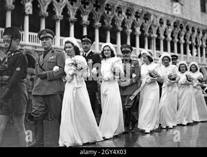 Nel 1939, a Venezia si sono svolte diverse nozze. Nella foto, le spose, accompagnate dai loro padri (ufficiali militari di alto rango), stanno camminando verso la Basilica di San Marco attraverso Piazza San Marco. Davanti c'è un ragazzo dell'Opera Nazionale Balilla. Sullo sfondo si trova il Palazzo Ducale. [traduzione automatizzata] Foto Stock