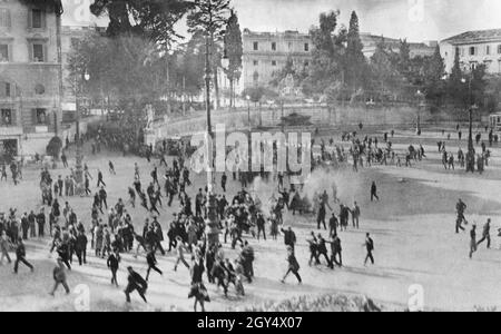 Scontri e rivolte scoppiarono a Roma nel 1924 il 4 novembre, giorno delle celebrazioni della Giornata della Vittoria. La foto mostra un violento confronto in Piazza del Popolo. Generale Giuseppe Garibaldi il giovane veniva dalla porta del Popolo con delle magliette rosse quando un distacco di fascisti fuori città li attaccò. Al centro del quadro c'è il fumo delle pistole sparate, su cui la folla fuggì. La Fontana del Nettuno è visibile sullo sfondo. La Giornata della vittoria ha commemorato l'armistizio dell'Italia con l'Austria-Ungheria il 4 novembre 1918. [traduzione automatizzata] Foto Stock