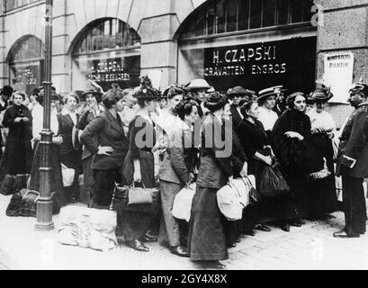 Un gruppo di donne attende fuori da una fabbrica di abbigliamento a Berlino nelle prime settimane della guerra del 1914, sotto la guardia di un ufficiale di polizia, per essere assegnato lavoro di emergenza. [traduzione automatizzata] Foto Stock