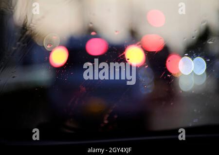 La pioggia cade sul parabrezza e le luci del bokeh dalle automobili che precedono. Immagine astratta. Foto Stock