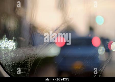 Luci bokeh e gocce di pioggia sul parabrezza. Immagine astratta. Foto Stock
