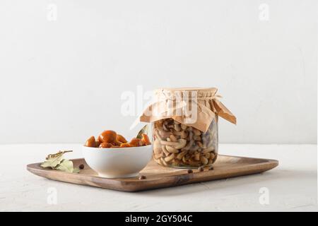 Funghi agarici al miele sottaceto fatti in casa e vasetto di vetro con spezie, foglia di alloro su sfondo bianco. Primo piano. Foto Stock