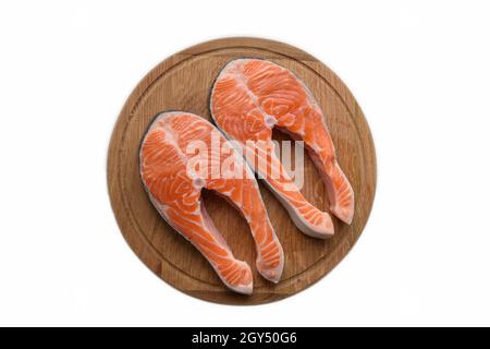 Due bistecche di pesce rosso crudo giacciono su una tavola rotonda di taglio di legno marrone. Su sfondo di ritaglio bianco Foto Stock