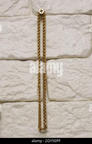 Catena in oro appesa a una vite su una parete in mattoni decorativi di colore chiaro al centro del telaio Foto Stock