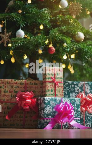 Scatole di Natale colorate regalo su pavimento in legno in sfondo sfocato albero Foto Stock