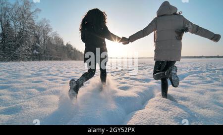 Le ragazze allegre corrono attraverso il campo coperto di neve. Foto Stock