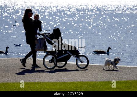 Londra, Inghilterra, Regno Unito. Kensington Gardens: Giovane donna con suo figlio e un cane che cammina vicino al lago, in silhouette Foto Stock