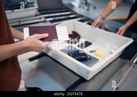 Il passeggero che detiene il passaporto contro oggetti personali, liquidi e computer portatile in contenitore al controllo di sicurezza dell'aeroporto. Foto Stock