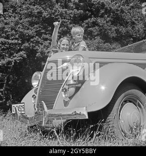 Eine junge Frau und ein Junge an der Kühlerhaube eines Automobils, Deutschland 1930er Jahre. Una giovane donna e un ragazzo al cofano del motore di un'auto, Germania 1930s. Foto Stock