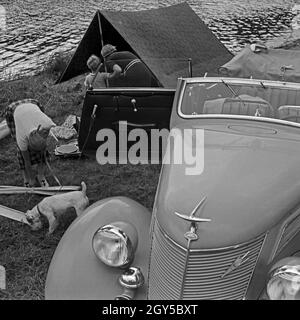 Zwei Frauen packen die Campinausrüstung zusammen in einen Ford V8 nach einem Tag am See, Deutschland 1930er Jahre. Due donne di imballaggio del materiale da campeggio in una Ford V8 dopo un giorno di ferie in un lago, Germania 1930s. Foto Stock