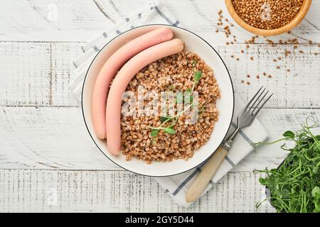 Porridge di grano saraceno bollito, salsicce di carne e microgreens di piselli in un piatto bianco per la colazione o il pranzo dei bambini su sfondo grigio pietra. Idea per una sim Foto Stock