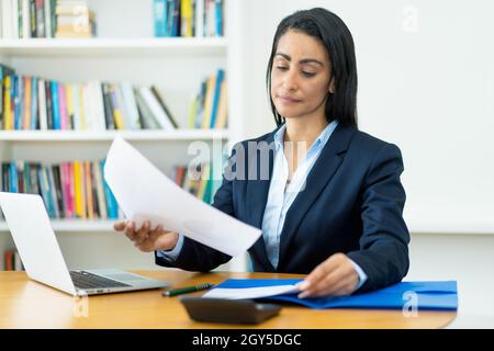 Donna d'affari ispanica matura che lavora con documenti alla scrivania in ufficio Foto Stock