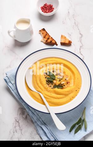 Zuppa tradizionale di zucca con consistenza cremosa e setosa con foglie di salvia e pepe rosso in piatto bianco o ciotola. Sfondo grigio chiaro. Spazio di copia. Mock up. Foto Stock