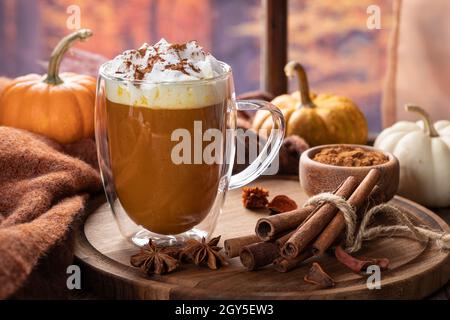 Latte di zucca speziata con bastoni di cannella e zucche da una finestra con sfondo autunno Foto Stock