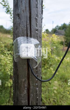 La presa elettrica con un filo, protetto dall'umidità da una visiera trasparente, è fissata a un vecchio palo in legno, all'aperto. Foto Stock