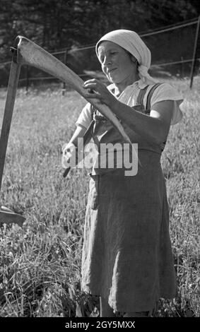 Eine Bäuerin schärft ihre sense, Deutschland 1940er Jahre. Una donna contadina che affilava la lama della sua falce, la Germania anni quaranta. Foto Stock