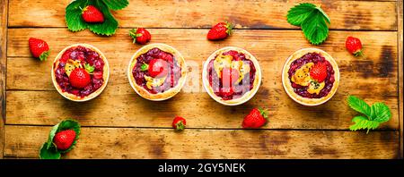 Deliziosi tartlet con marmellata di frutti di bosco.Cake con fragole su rustico sfondo di legno Foto Stock