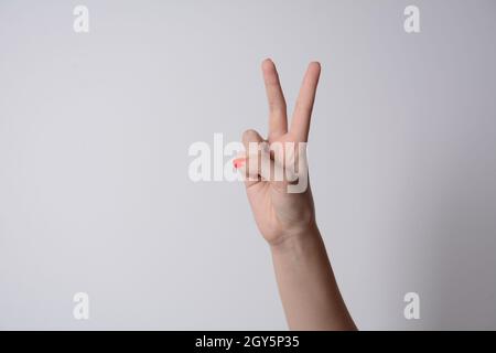 Donna alzando due dita in su sulla mano è mostra la lotta di forza di pace o simbolo di vittoria e lettera V in linguaggio dei segni su sfondo bianco Foto Stock