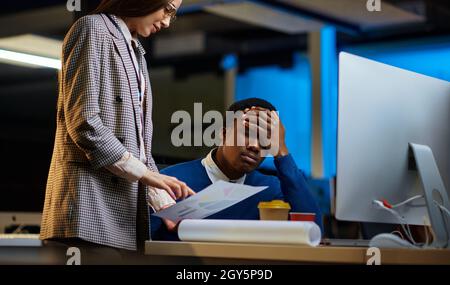 I dirigenti stanchi lavorano in ufficio notturno. Lavoratori di sesso maschile e femminile assondati, interni scuri del business center sullo sfondo, ambiente di lavoro moderno Foto Stock