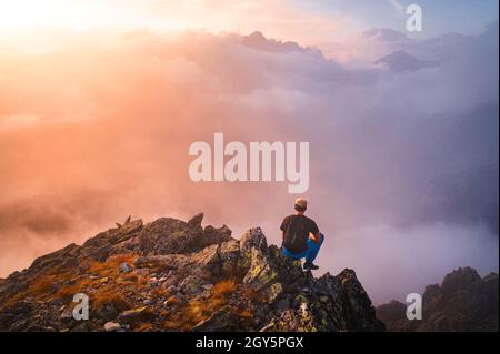 L'escursionista in nero siede da solo sulla cima della roccia. Meravigliosa escursione in montagna, vista posteriore di zaino in spalla sedersi sul bordo. Foto Stock