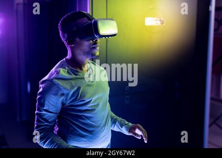 Tecnico informatico africano americano maschile che indossa il visore vr e lavora nella sala server Foto Stock