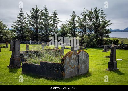 Un'antica tomba doppia abbandonata nel cimitero, circondata da piccole lapidi. Erba verde, alberi sullo sfondo. Foto Stock