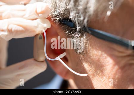 Dottore che inserisce l'udito nell'orecchio dell'uomo Foto Stock