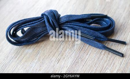 Un soggetto di lacci piatti blu scuro con punte sottili per le scarpe arrotolate e isolate su uno sfondo di legno. Accessorio elegante Foto Stock