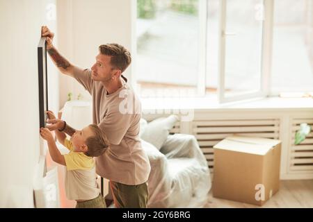 Vista laterale ritratto di padre e figlio appeso immagini sul muro mentre si sposta in nuova casa, spazio copia Foto Stock