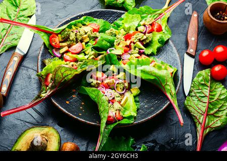 Insalata di avocado, pomodoro con salsa all'aglio in foglie di bietole. Insalata di vitamina estiva in piatto Foto Stock